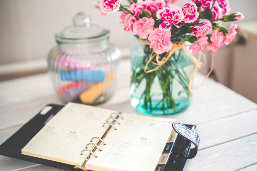 Desk with flowers, organiser and chalks. Make sure you plan your business blogging schedule thoroughly.