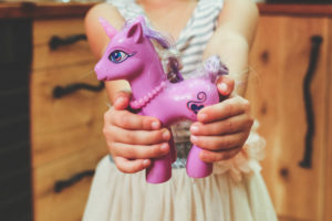 little girl holding a pink toy unicorn